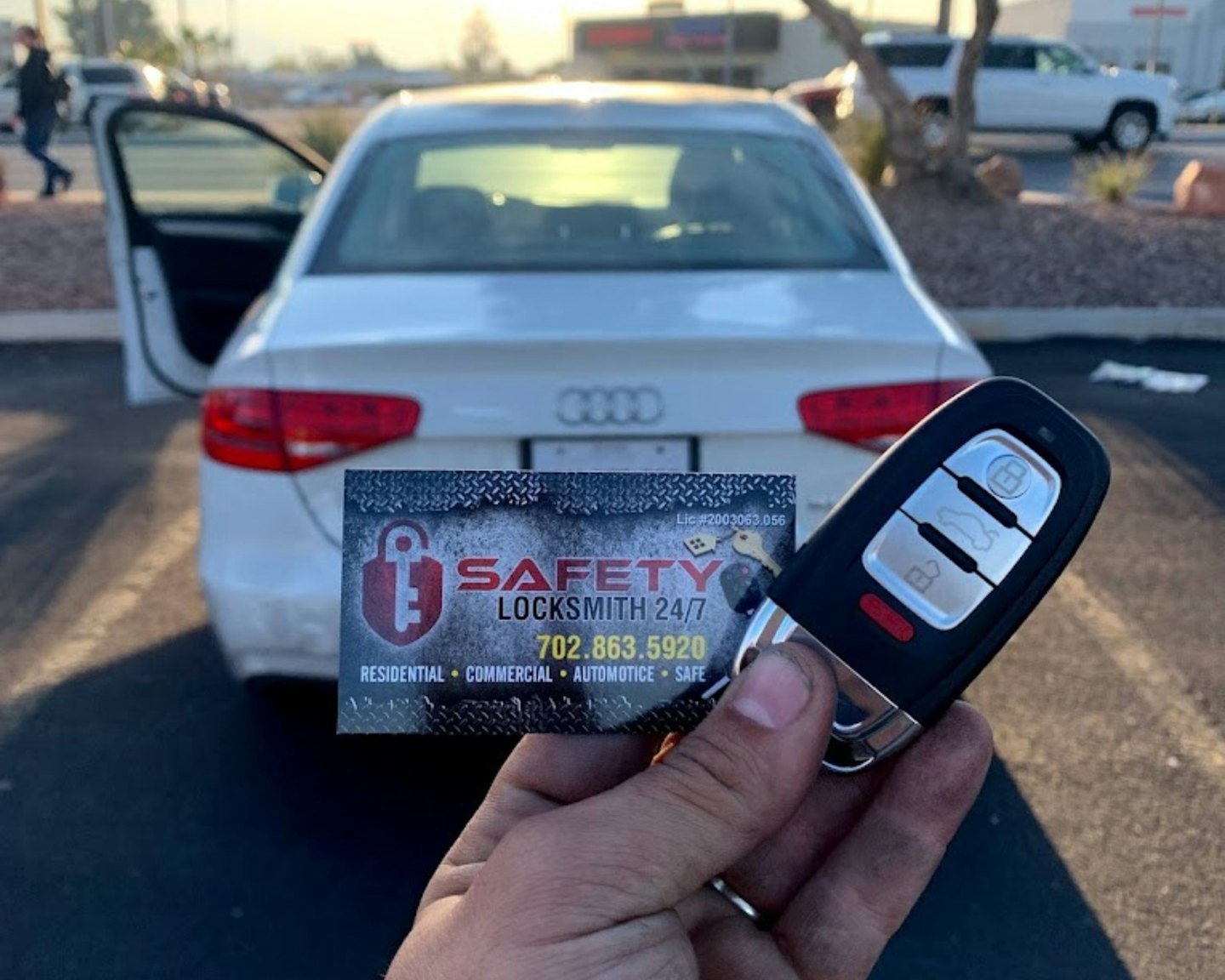 Hand holds car key fob and locksmith business card by open car door.