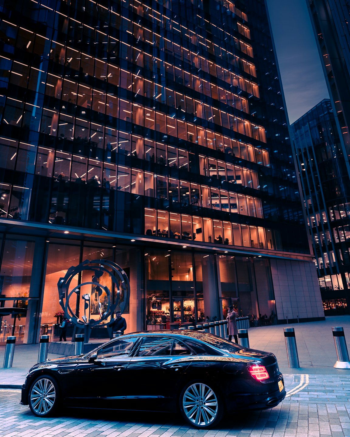 A luxury sedan parked before a modern glass corporate skyscraper.